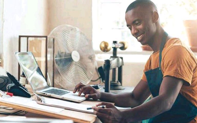 A Nigerian entrepreneur working on a laptop while managing small business products, representing modern side hustles in 2026.